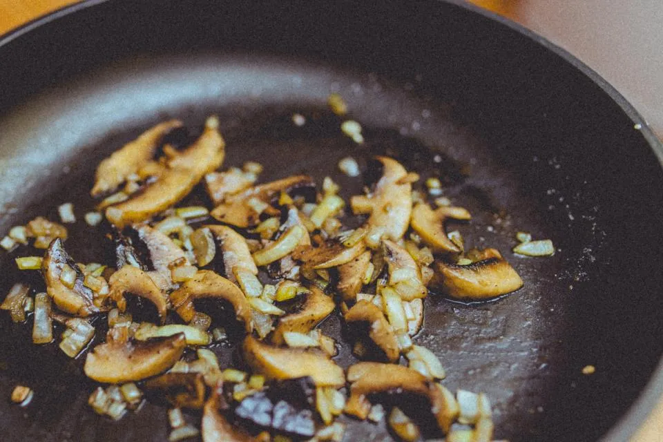 Sliced mushrooms sauteing in a dark skillet
