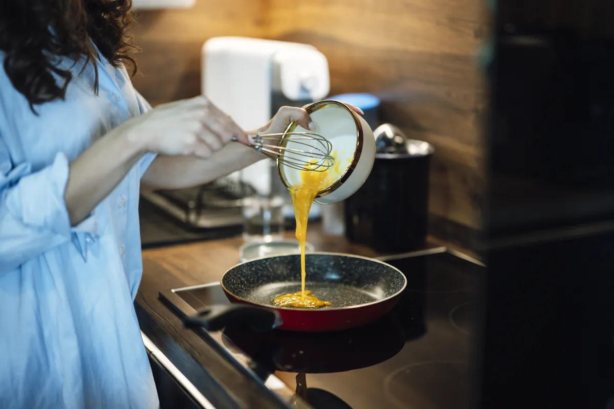 Person pouring beaten eggs into a frying pan on a stove